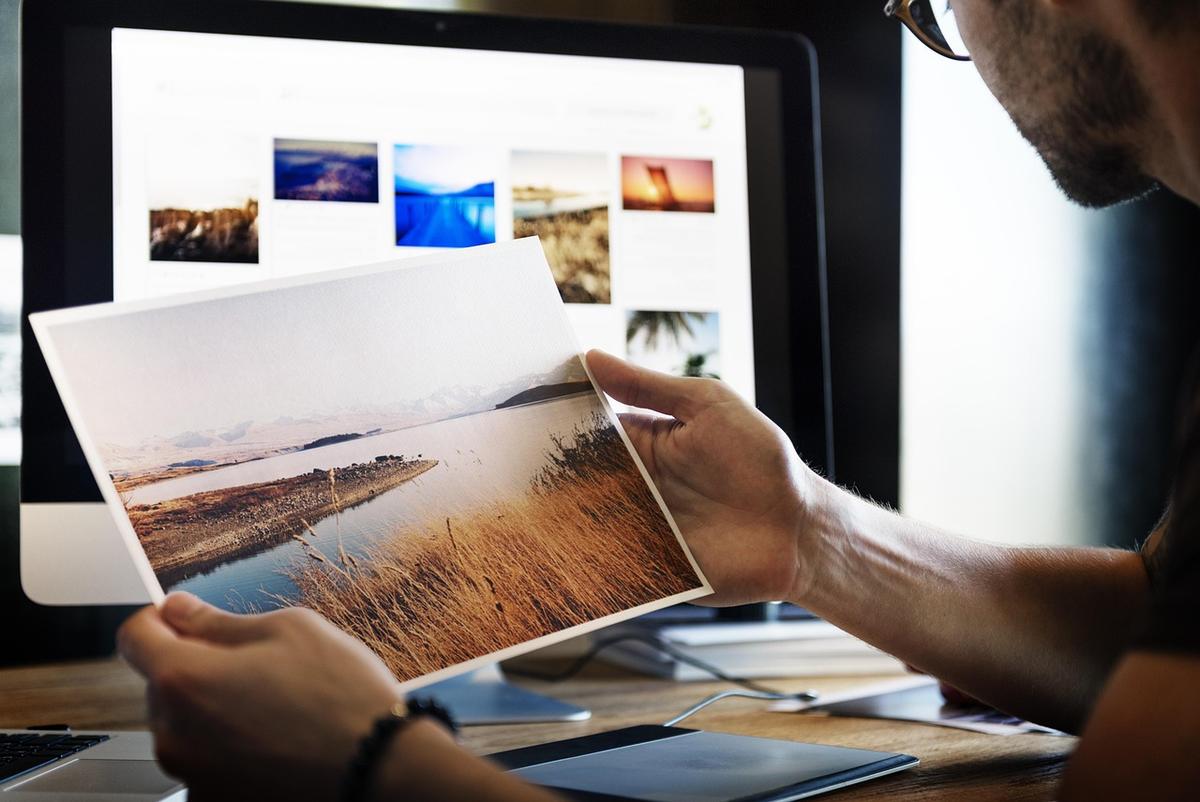 Homme examinant et triant des photographies imprimées à côté d'un écran affichant une galerie d'images