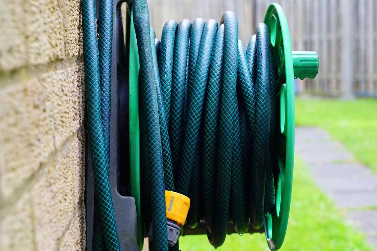 Un tuyau vert enroulé sur un rouleau fixé à un mur de brique Un tuyau vert enroulé sur un rouleau fixé à un mur de brique