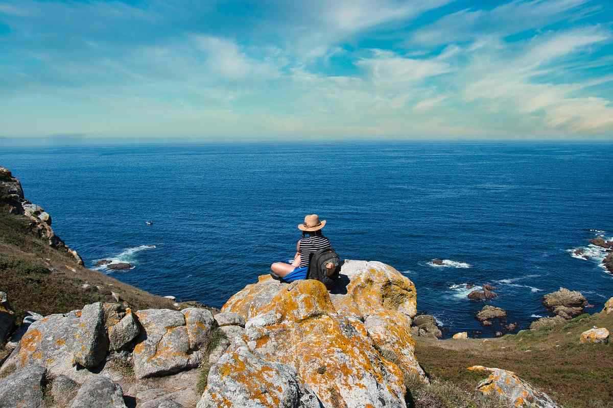 Personne assise sur des rochers, contemplant la mer sous un ciel bleu
