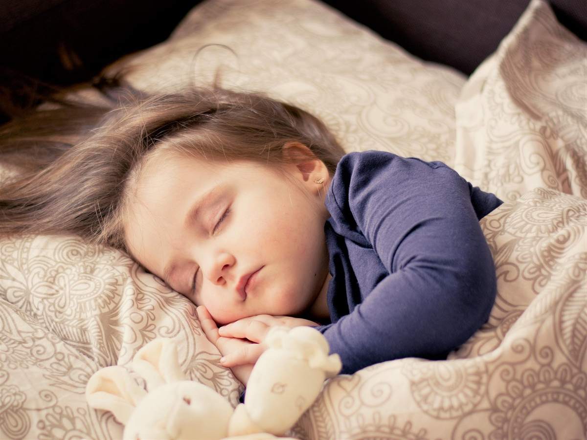 Enfant paisible endormi sur oreiller, serrant peluche dans un lit douillet