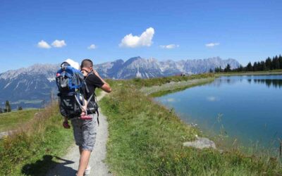 Un randonneur porte un enfant dans un sac à dos sur un sentier