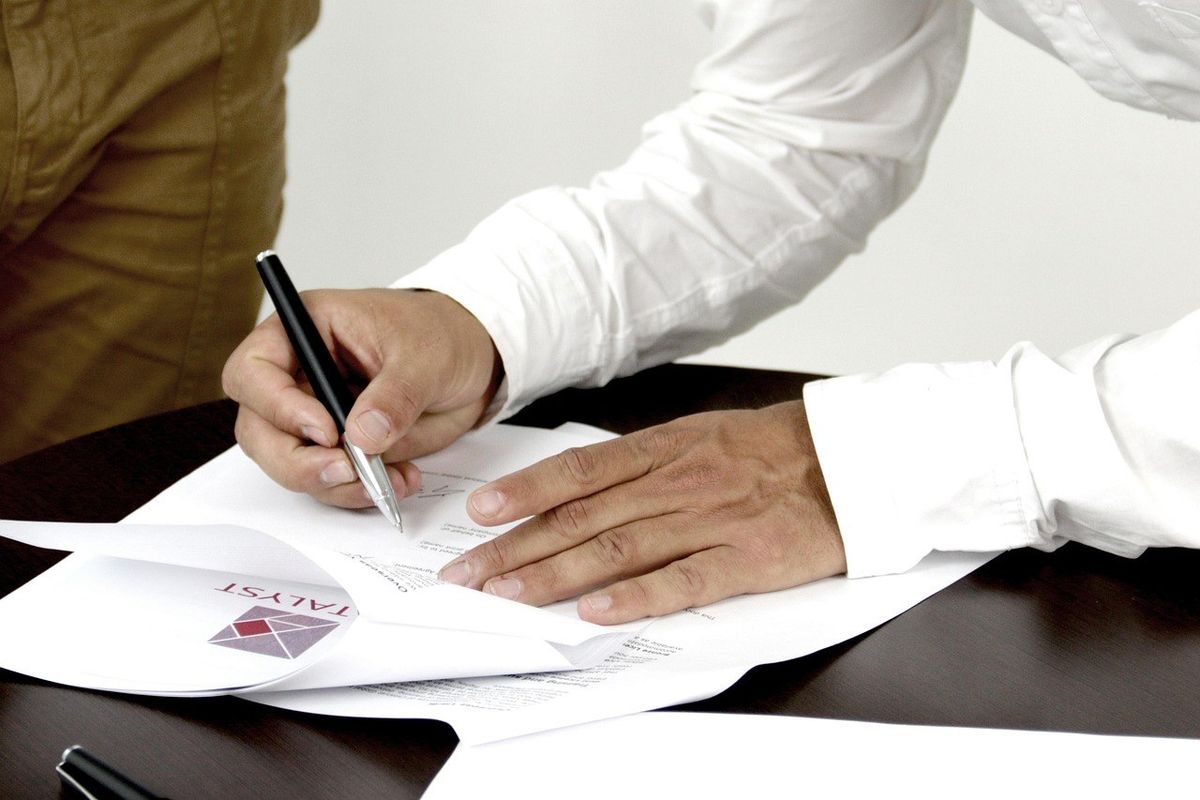 Main écrivant sur un document avec un stylo, une autre main posée dessus