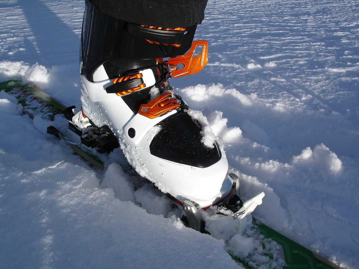 Botte de ski blanche et noire avec attaches orange sur pied posé sur neige