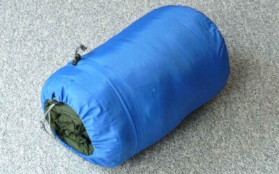 Sac de couchage bleu compressé avec lien de serrage, posé sur sol gris