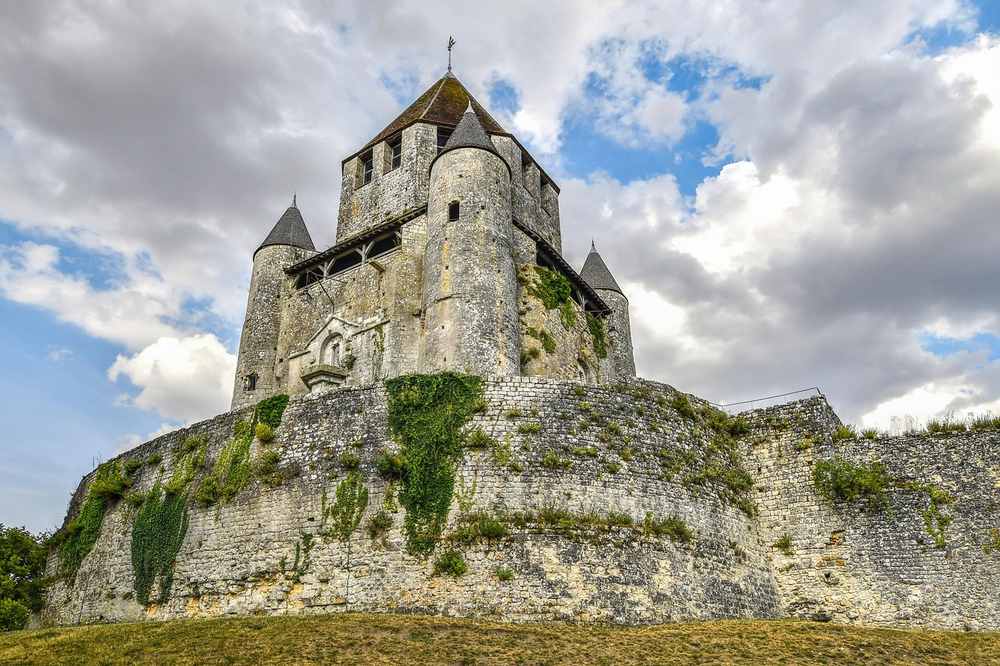 Château fort médiéval dominant une colline herbeuse sous ciel couvert