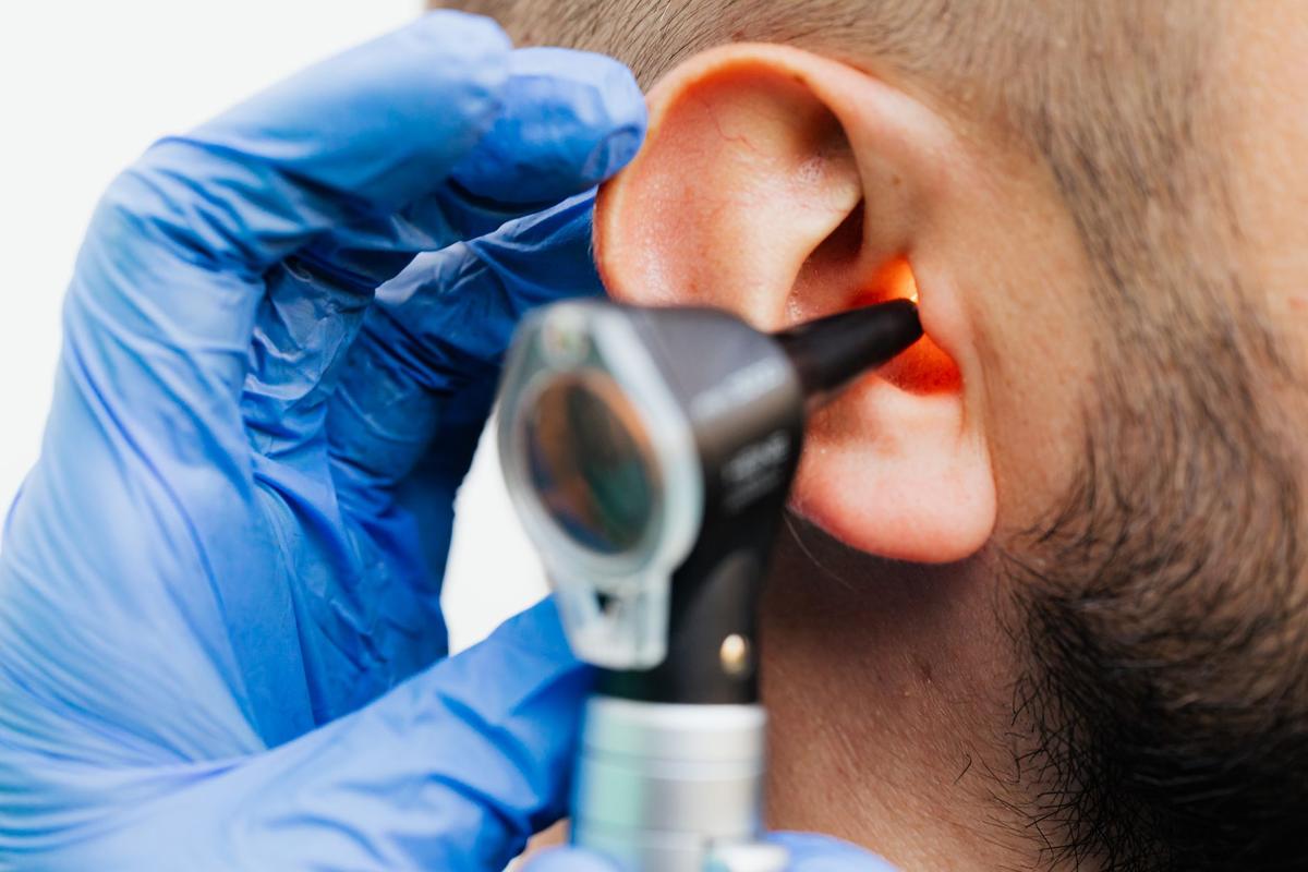 Une main gantée examine l'oreille avec un otoscope
