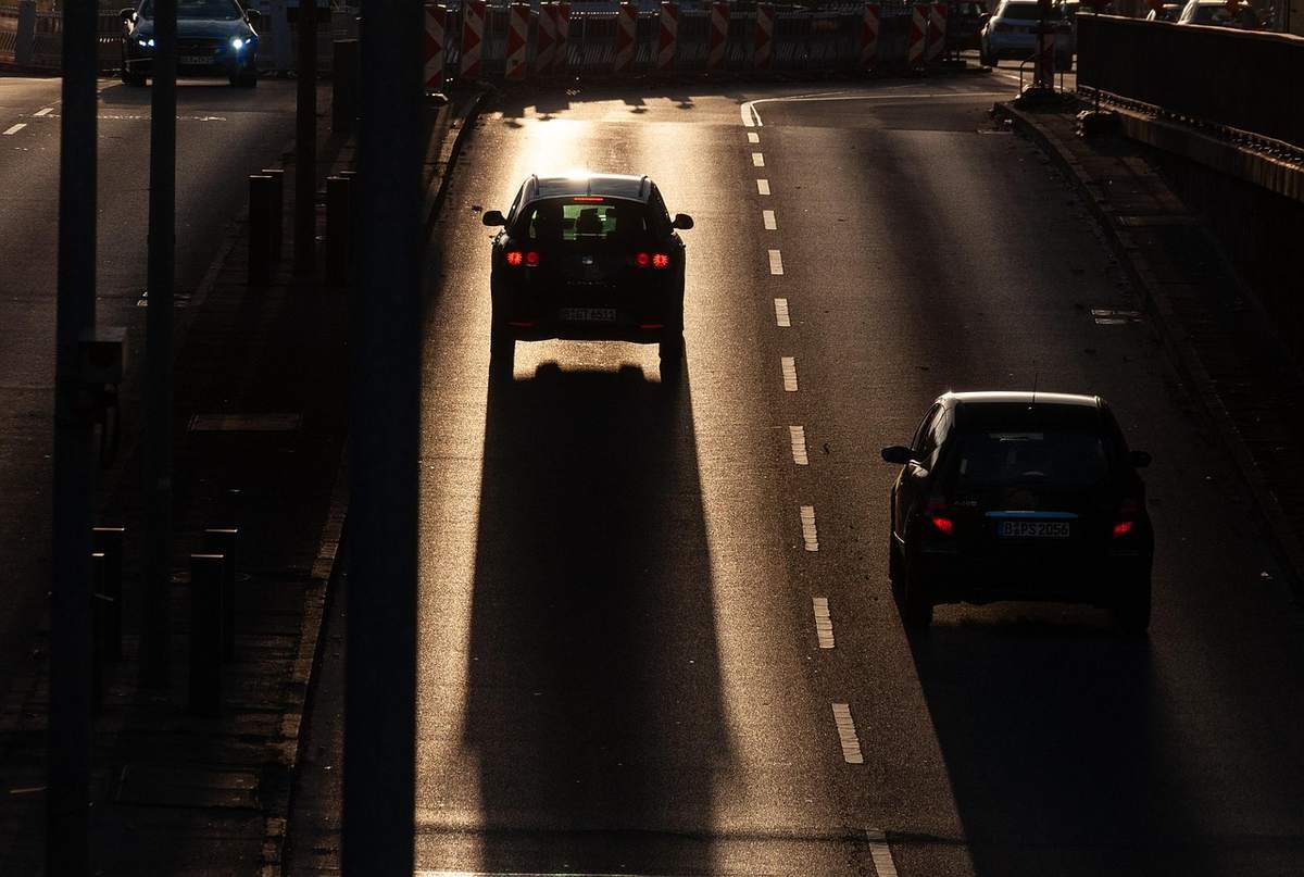 Deux voitures circulent sur une autoroute éclairée par le soleil couchant